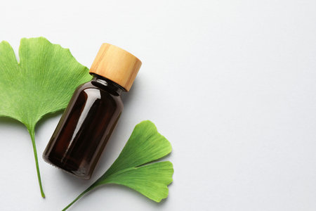 Ginkgo biloba leaves and bottle on light gray background, flat lay. Space for text