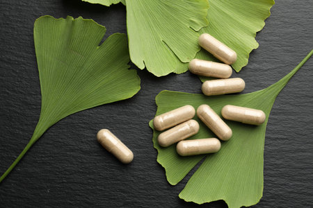 Ginkgo biloba leaves and pills on dark textured table, flat layの写真素材