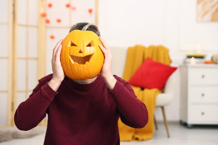 Halloween celebration. Man holding pumpkin with carved spooky face indoors, space for textの写真素材