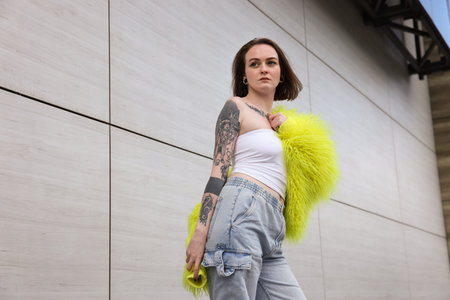 Young woman with piercings, tattoos and stylish clothes outdoors, low angle view. Space for textの写真素材