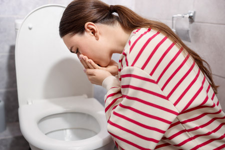 Woman suffering from nausea over toilet bowl in bathroomの写真素材