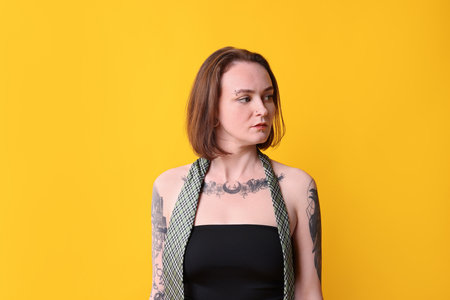 Young woman with piercings, tattoos and stylish clothes posing on yellow backgroundの写真素材