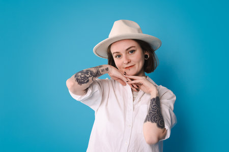 Young woman with piercings, tattoos and stylish clothes posing on light blue backgroundの写真素材