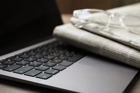 Newspapers, laptop and glasses on gray table, closeup