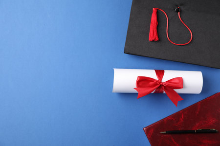 Diploma, graduation hat and stationery on blue background, flat lay. Space for textの写真素材