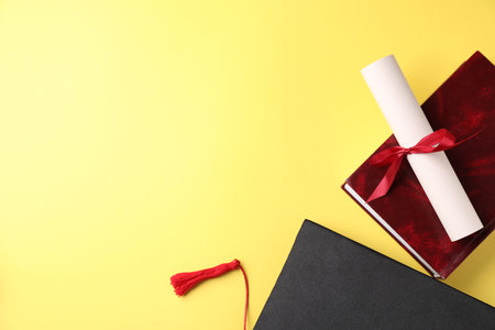 Diploma, graduation hat and book on yellow background, flat lay. Space for textの写真素材