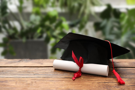 Diploma and graduation hat on wooden table outdoors, closeup. Space for textの写真素材