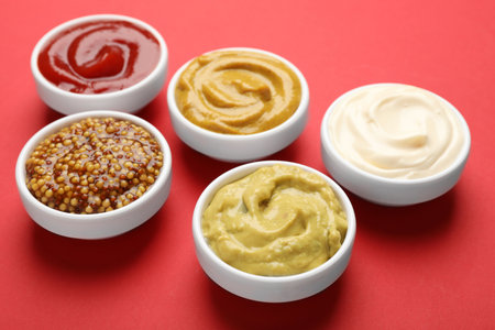Different sauces in bowls on red background, closeupの写真素材