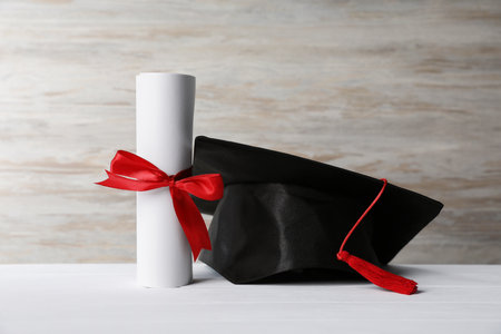Graduation hat and diploma on white wooden tableの写真素材