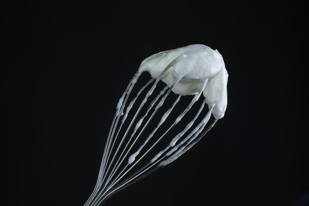 Whisk with whipped egg whites on black backgroundの写真素材
