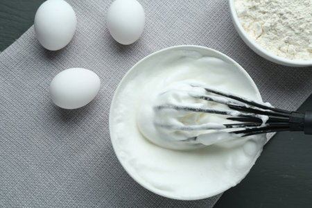 Whipped whites in bowl, flour and eggs on gray wooden table, flat layの写真素材