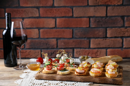 Tasty bruschettas with cheese, tomatoes, sausages, shrimps, lemon and red wine on wooden table against brick wall, closeup. Space for textの写真素材