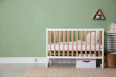Blurred view of crib, basket and decor near light green wall, space for text. Stylish baby's room interiorの写真素材