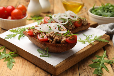 Delicious bruschettas with tuna, tomatoes, onion and arugula on wooden table, closeupの写真素材