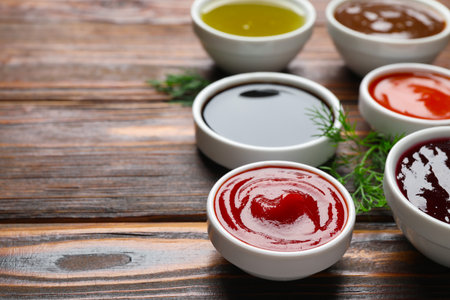 Different sauces in bowls with fresh dill on wooden table, closeup. Space for textの写真素材