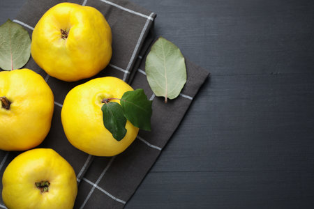 Ripe quinces and green leaves on black wooden table, top view. Space for textの写真素材