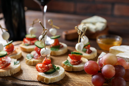 Tasty bruschettas with cheese, cucumber, parsley and grapes on wooden board, closeupの写真素材