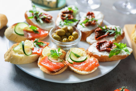 Tasty bruschettas with salmon, cucumber, sun dried tomatoes and olives on gray textured table, closeupの写真素材