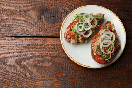 Bruschettas with tuna, tomatoes, onion and arugula on wooden table, top view. Space for textの写真素材