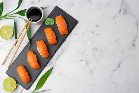 Delicious nigiri sushi with salmon, wasabi, chopsticks, soy sauce and leaves on light marble table, flat lay. Space for textの写真素材