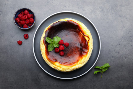 Tasty Basque cheesecake, raspberries and mint on gray textured table, flat lay