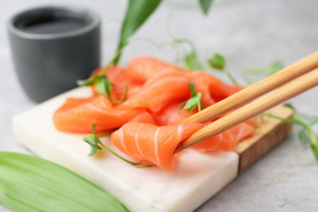 Taking fresh salmon sashimi with chopsticks from board at gray table, closeupの写真素材