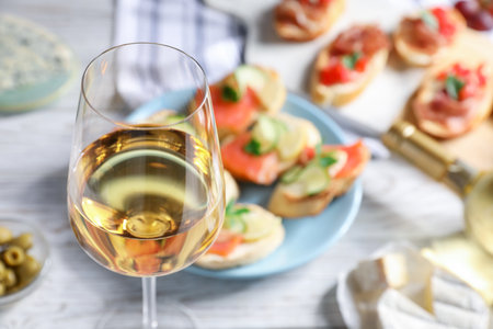 Glass of white wine and tasty bruschettas on white wooden table, selective focusの写真素材