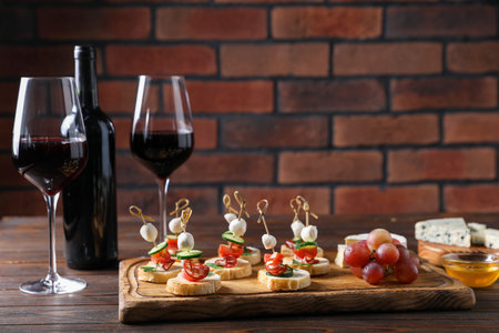Tasty bruschettas with cheese, cucumber, sausages and red wine on wooden table against brick wall, closeup. Space for textの写真素材