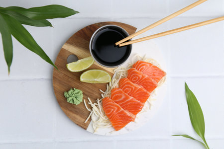 Fresh salmon sashimi with sliced radish, wasabi, lime and soy sauce on light tiled table, flat layの写真素材