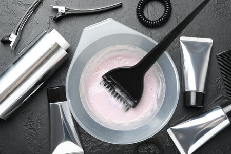 Hair dyeing product in bowl and different hairdresser's tools on black table, flat layの写真素材