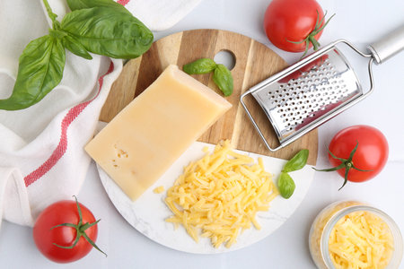 Grater, tomatoes, basil, grated and piece of cheese on white table, flat layの写真素材