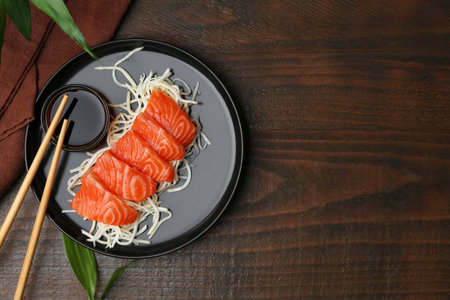 Fresh salmon sashimi with sliced radish, soy sauce and chopsticks on wooden table, flat lay. Space for textの写真素材