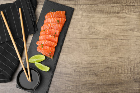 Fresh salmon sashimi with microgreens, lime and soy sauce served on wooden table, flat lay. Space for textの写真素材