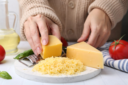 Woman grating cheese at white tiled table, closeupの写真素材