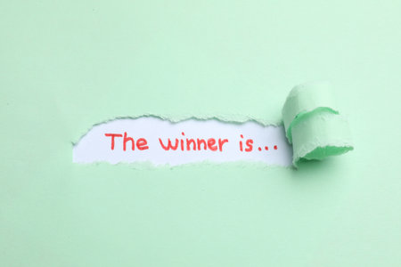 Phrase The Winner Is on white background, view through hole in torn pale green paperの写真素材