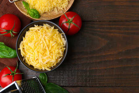 Grated cheese, grater, tomatoes and basil on wooden table, flat lay. Space for textの写真素材