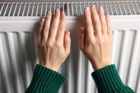 Woman warming her hands near radiator indoors, closeupの写真素材