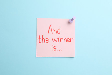 Sticky note with phrase And The Winner Is on light blue background, top viewの写真素材