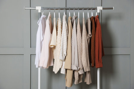 Different clothes hanging on rack near gray wall indoors