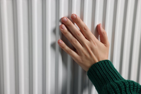 Woman warming her hand near radiator indoors, closeupの写真素材