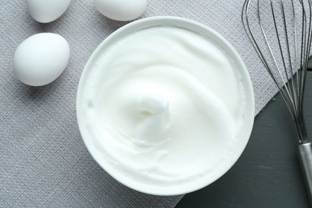 Whipped whites in bowl, eggs on gray wooden table, flat layの写真素材