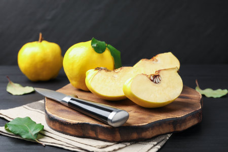 Ripe quinces, knife and green leaves on black wooden table, closeupの写真素材