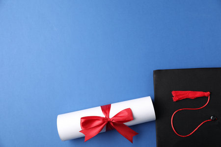 Diploma and graduation hat on blue background, flat lay. Space for textの写真素材