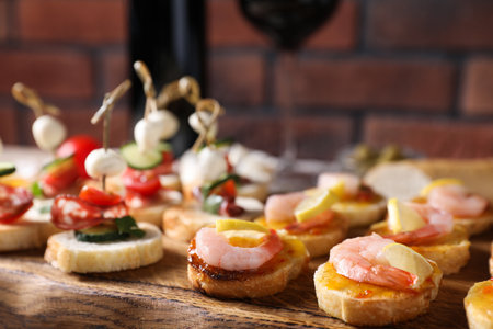 Tasty bruschettas with cheese, tomatoes, sausages, shrimps, sauce and lemon on wooden board against red brick wall, closeupの写真素材