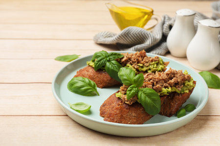 Delicious bruschettas with tuna, avocado and basil served on light wooden table, closeupの写真素材