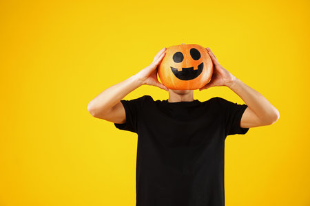 Halloween celebration. Man holding pumpkin with drawn spooky face on orange background, space for textの写真素材