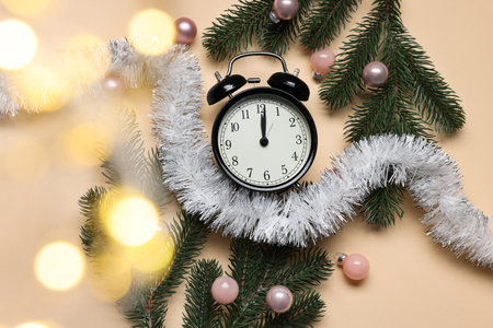 New Year greeting card. Alarm clock, fir tree branches, baubles and tinsel on beige background, flat...