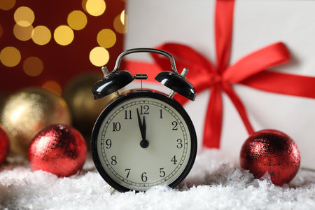 New Year celebration. Alarm clock and festive decor on artificial snow against blurred lights, closeupの写真素材