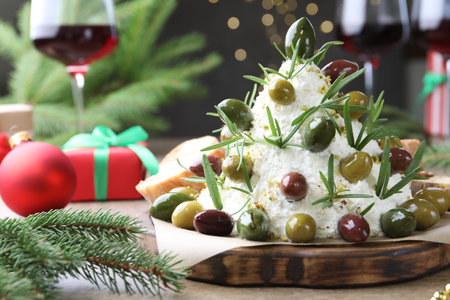 Delicious Christmas tree cheese ball with olives, rosemary and decor on wooden table against gray background with blurred lights, closeup. New Year's appetizerの写真素材