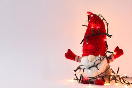 Funny Christmas gnome and festive lights on light gray background, closeup. Space for textの写真素材